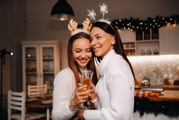 two girls in a cozy home environment with champagne in their hands at Christmas. Smiling girls drink champagne on a festive evening. - Foto, Imagen
