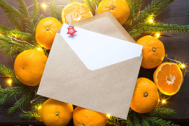 Envelope with a sheet of paper-a letter to Santa Claus, Copyspace on a Christmas background of tangerines, garlands, fir branches. Clothespin-star in place for notes. New year, wish list, dream, gifts - 写真・画像