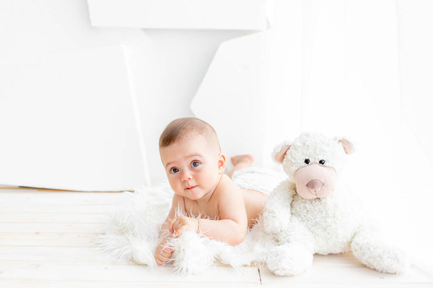 un bébé avec un ours en peluche est couché dans une pièce lumineuse - Photo, image