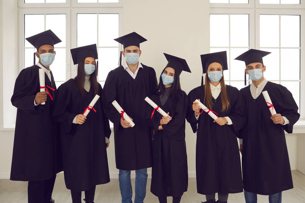 Group portrait of multiethnic university graduates in face masks holding their diplomas - Foto, Imagen