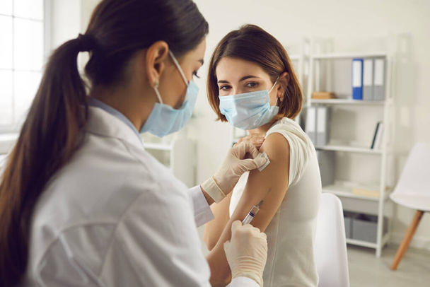 Young woman in face mask getting coronavirus or flu antiviral vaccine at the hospital - Photo, Image