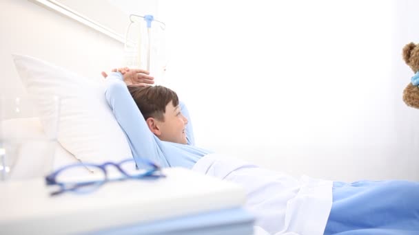 enfermera sonriente cuida de un niño acostado en la cama del hospital haciéndole una sorpresa dándole un osito de peluche - Metraje, vídeo