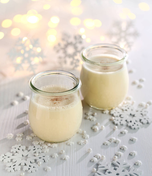 Festive eggnog sprinkled with nutmeg in glass dish on a light background. Delicious homemade drink and desert - Fotó, kép