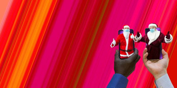 Afroamerikaanse en blank-witte handen die telefoons vasthouden met 2 kerstmannen. De kerstman heeft medische maskers op. Close-up op een rode achtergrond met verloop. - Foto, afbeelding
