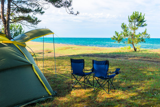 tente de camping et quelques chaises au bord de la mer à l'ombre des pins - Photo, image