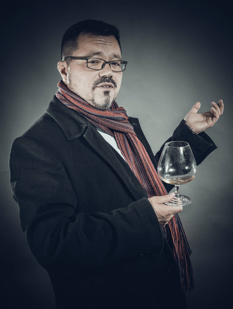 Solid cheerful man in coat and kerchief standing with glass of wine - Foto, afbeelding