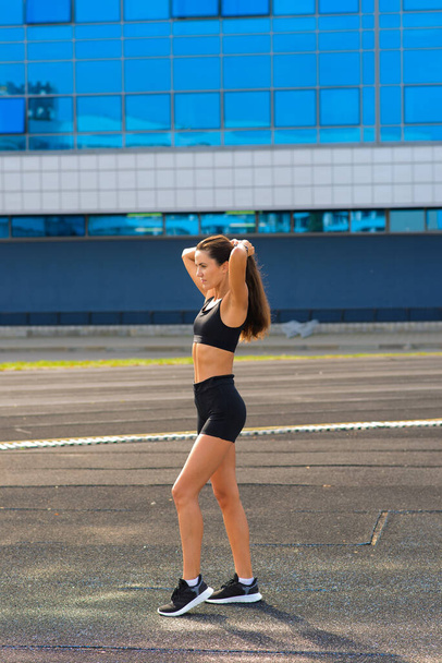 Mujer joven y saludable calentándose estirando los brazos en el estadio al aire libre, haciendo footing en el parque. - Foto, Imagen