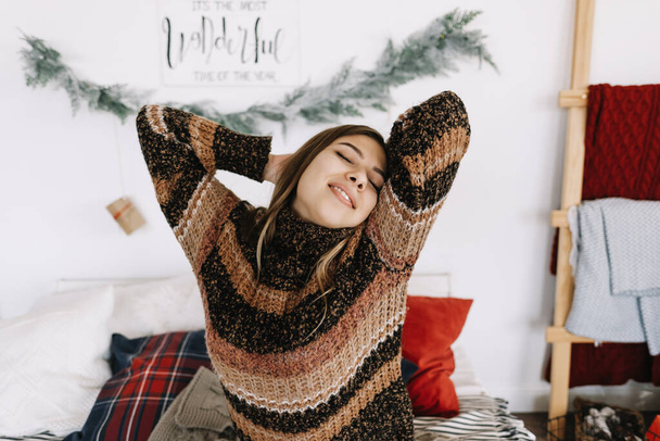 Happy young caucasian woman stretching in bed, waking up on Christmas morning. High quality photo - Фото, зображення