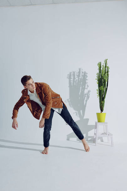 A man in fashionable clothes is dancing indoors near a flower in a pot - Foto, Bild