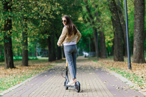 Junge schöne stilvolle Frau fährt Elektroroller im Herbst Park, ökologischen Transport - Foto, Bild