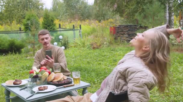 Een man maakt foto 's van zijn vrouw op een smartphone tijdens een picknick in de tuin. Meisje poseren. - Video