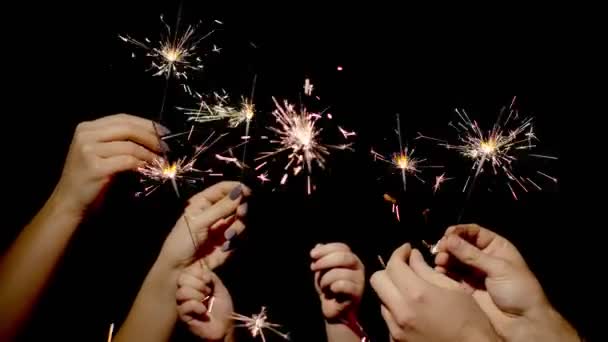 Lähikuva kädet pitämällä ja heiluttaen bengal palava sparklers edessä musta tausta - Materiaali, video