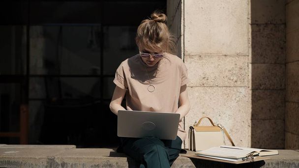 Young woman in sunglasses with laptop preparing for the exam outside - 写真・画像