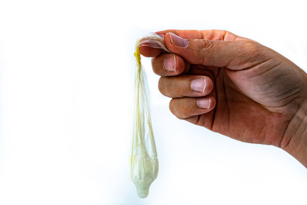 Männliche Hand hält ein gebrauchtes Kondom mit Sperma darin, Knoten auf dem Kondom. Isoliert auf weiß. . Hochwertiges Foto - Foto, Bild