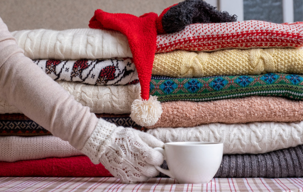 Veel truien en truien Verschillende kleuren gevouwen in twee stapels en hand met kopjes koffie. - Foto, afbeelding