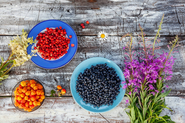 Des baies sauvages estoniennes fraîchement cueillies comme les myrtilles, les bleuets et les fraises sauvages sur une table en bois rustique, - Photo, image