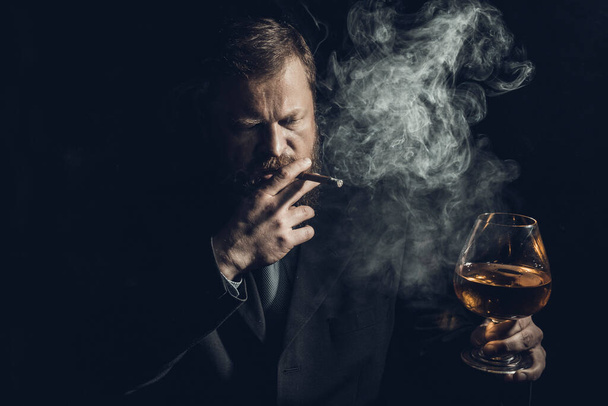 Solid confident bearded man in suit with glass of whisky and cigar with fume - Foto, imagen