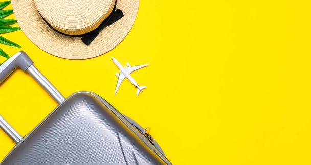 Nyári háttérasztal. Bőrönd, napszemüveg pálmalevéllel és szalmakappal, fehér sík utazási kompozícióban, sárga háttérrel. Fénymásolás, nyári vakáció és üzleti utazási koncepció - Fotó, kép
