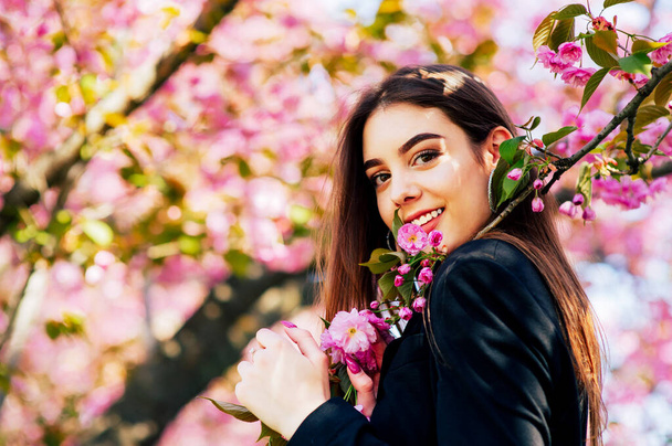 дівчина з довгим волоссям насолоджується красою весняної природи біля квітучого дерева сакури
. - Фото, зображення