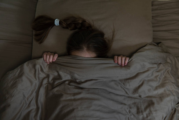 Girl with dark hair hides in bed with fear. high quality - Foto, Imagem