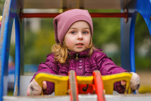 Ragazzina attiva nel parco giochi. Bambina bambina nel parco giochi. Bambino in giacca viola - Foto, immagini