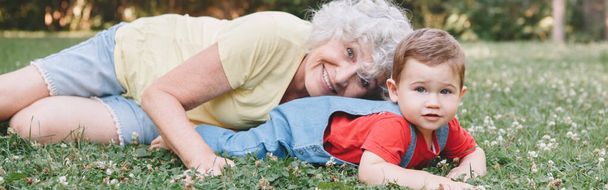 Бабушка лежала на траве с внуком на заднем дворе. Старушка с ребенком веселится, проводя время вместе на свежем воздухе. Заголовок веб-баннера. - Фото, изображение