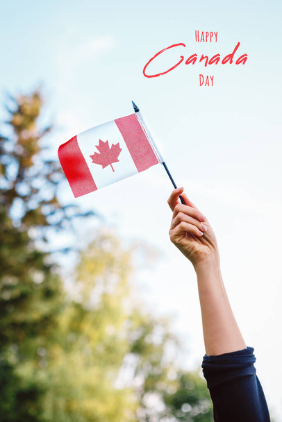 Cartão feliz do Dia do Canadá com texto. Fechar o braço da mão humana mulher acenando bandeira canadense contra o céu azul. Orgulhoso cidadão homem celebrando o Dia Nacional do Canadá no dia 1 de julho ao ar livre.  - Foto, Imagem