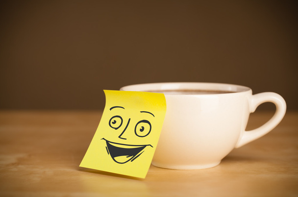 Post-it note with smiley face sticked on a cup - Valokuva, kuva