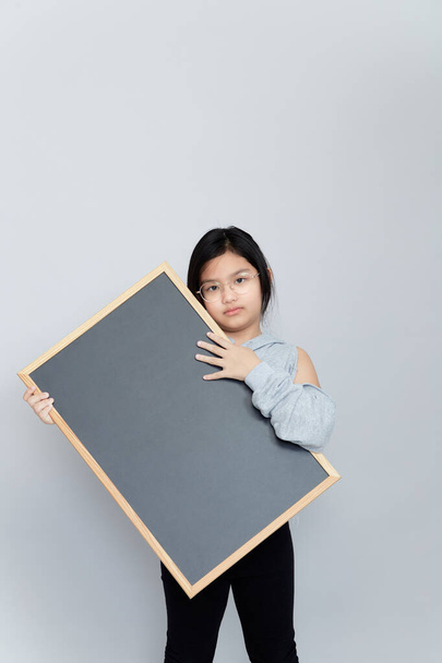 Ένα μικρό κορίτσι κρατά ένα κενό chalkboard θέση για κοινοποίηση. Διάβασε αυτή την ανακοίνωση. Ενημέρωση για το γεγονός. Χαριτωμένη μαθήτρια με μαυροπίνακα. Διαφήμιση. - Φωτογραφία, εικόνα