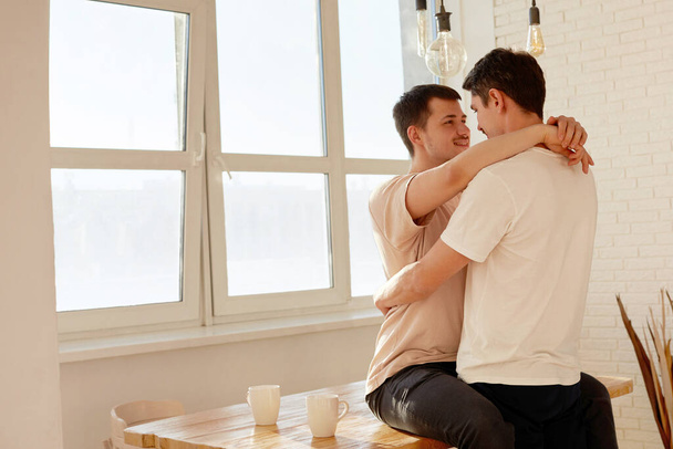 Beautiful cute gay couple, LGBT couple, in bright kitchen - Photo, Image