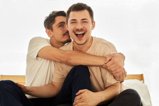 Porträt Nettes männliches queeres Paar zu Hause sitzt auf einem Sofa und blickt in die Kamera - Foto, Bild