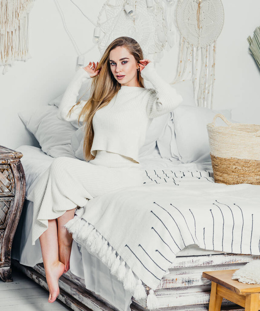 mujer joven con el pelo rubio largo y lujoso en la cama en el dormitorio en tonos blancos interior - Foto, imagen