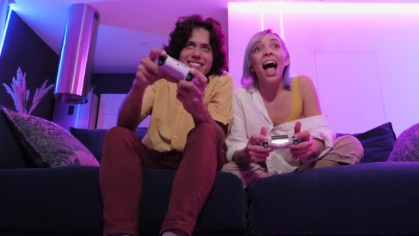 Mosolygó pár kezében gamepad játszik videojáték otthon. Alacsony látószögű kép arról, hogy a fiatalok mennyi időt töltenek együtt a világjárvány miatti elszigeteltség alatt.. - Felvétel, videó
