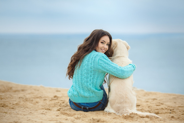 Portrait of beautiful young woman playing with dog on the sea shore - Photo, image