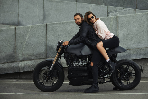 para moda siedzi na motocyklu, kamienna ściana na tle. młody mężczyzna i kobieta z nowoczesnym motocyklem - Zdjęcie, obraz