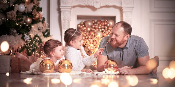 Padre de familia y sus dos niñas Acuéstese en el cuadros en la casa decorada para la Navidad, el concepto de unas vacaciones familiares de Navidad y Año Nuevo. Foto de alta calidad - Foto, imagen