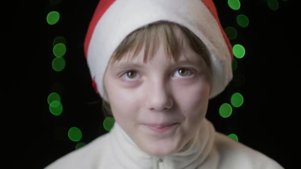 menina feliz no chapéu de Papai Noel olha para a câmera. Ano Novo, Natal comemorando - Filmagem, Vídeo