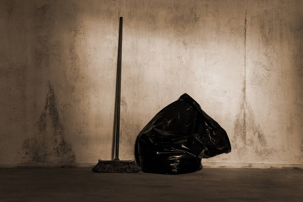 Natural old broom and big black plastic bag at the wall in house repair time. - Photo, Image