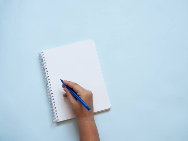 Carnet spirale vierge avec main caucasienne tenant un stylo bleu prêt à écrire. Fond bleu avec espace de copie. Réflexion, écriture, créativité et concept de retour à l'école. - Photo, image