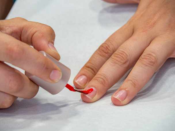 Kobieta malująca paznokcie czerwonym lakierem do paznokci. Zabieg kosmetyczny dla uroku i elegancji. Zamknij damskie dłonie. - Zdjęcie, obraz