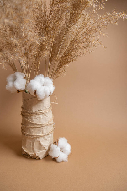 Bouquet of pampas grass and cotton flowers on beige background in craft vase. Boho style bouquet. Eco flower composition  - Photo, Image
