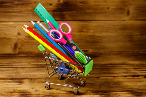 Buying school supplies. Shopping cart with school supplies on a wooden background. Back to school concept - Foto, Imagen
