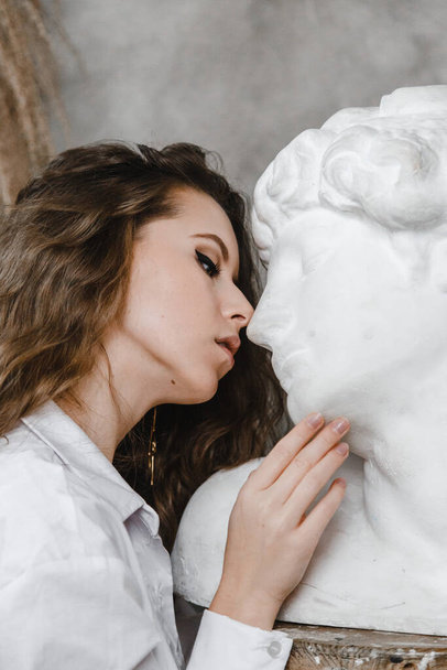Beautiful curly girl kissing white plaster head - Fotó, kép