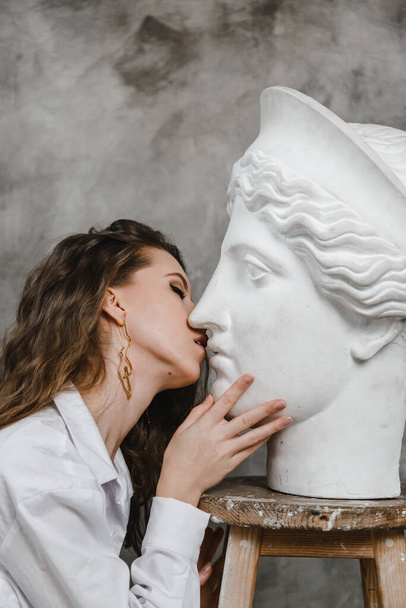 Schöne lockige Mädchen küssen weißen Gipskopf - Foto, Bild