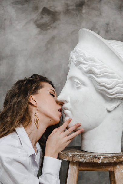 Schöne lockige Mädchen küssen weißen Gipskopf - Foto, Bild
