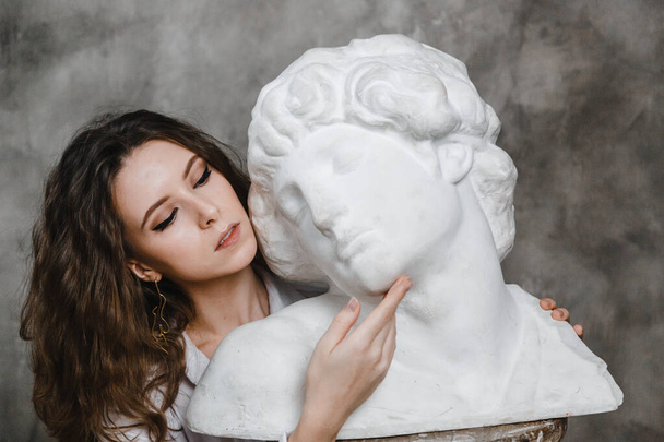 beautiful curly girl sitting hugging with plaster statue - Fotó, kép