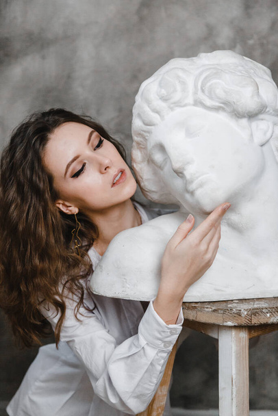 beautiful curly girl sitting hugging with plaster statue - Photo, image