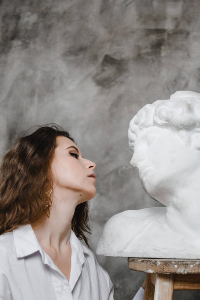 beautiful curly girl sitting hugging with plaster statue - Photo, Image