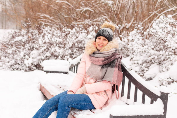 Молодая девушка сидит на скамейке в снежном парке. - Фото, изображение