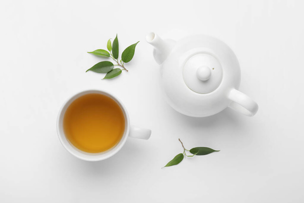 чайник, чашка чая и зеленые листья на белом фоне - Фото, изображение